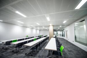 Alt Tab Room in Code Node set up for a talk, with rows of black and green chairs at long desks.